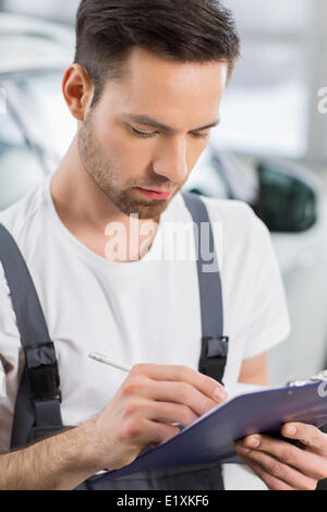 Mécanicien automobile mâle writing on clipboard in workshop Banque D'Images