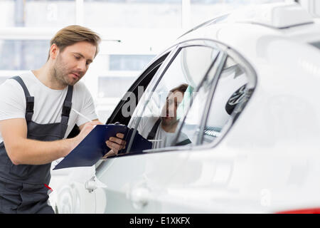 Mécanicien automobile writing on clipboard lors de l'examen de voiture dans l'atelier de réparation Banque D'Images