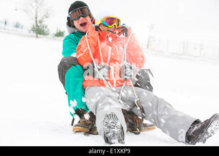 Jeune couple excité Sledding in snow Banque D'Images