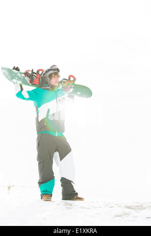 Toute la longueur de young man carrying snowboard dans la neige Banque D'Images