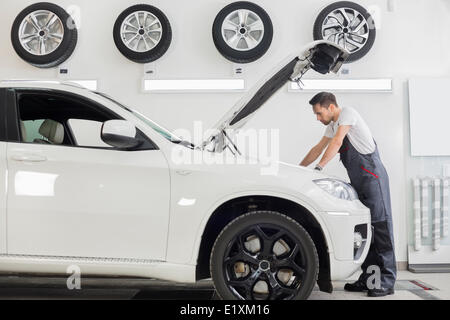 Vue latérale sur toute la longueur de l'examen de mécanicien moteur voiture mâle dans l'atelier de réparation Banque D'Images