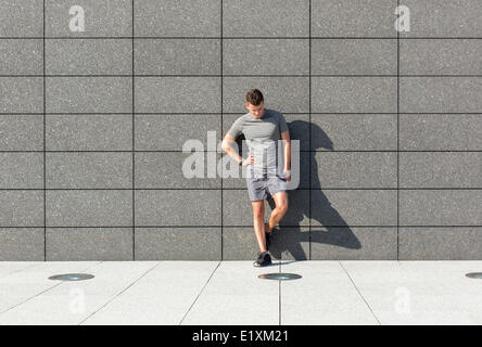 Toute la longueur de fatigué sporty man leaning on mur carrelé Banque D'Images