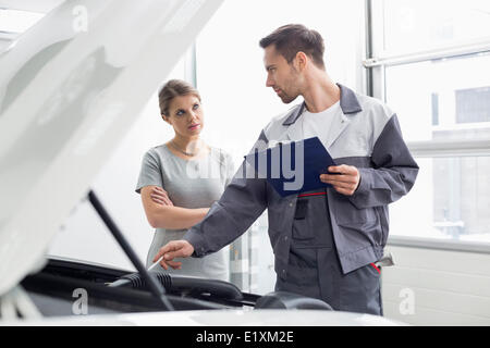 Ingénieur jeune mâle à femelle moteur voiture expliquant en atelier client Banque D'Images