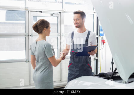 Ingénieur maintenance souriant shaking hands with female client en atelier de réparation de voiture Banque D'Images