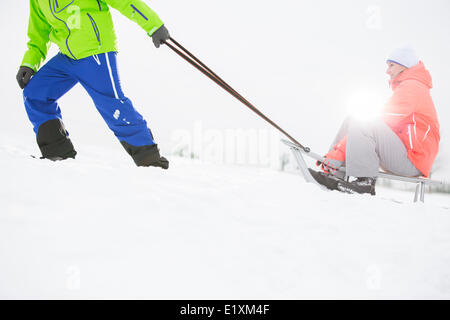 La section basse de l'homme donnant traîneau à femme dans la neige Banque D'Images