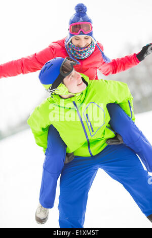 Happy young man giving piggyback ride to woman in snow Banque D'Images