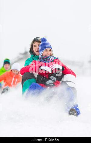 Jeunes amis excités Sledding in snow Banque D'Images