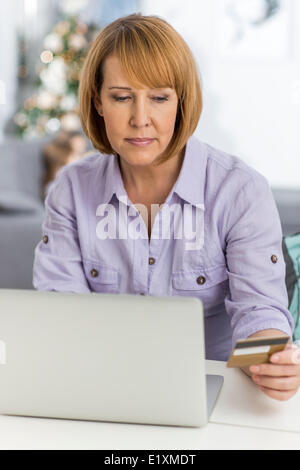 Mature Woman shopping online à la maison durant les fêtes de Noël Banque D'Images