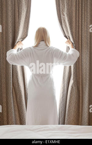 Vue arrière du jeune femme en peignoir chambre les rideaux à ouverture chambre d'hôtel Banque D'Images