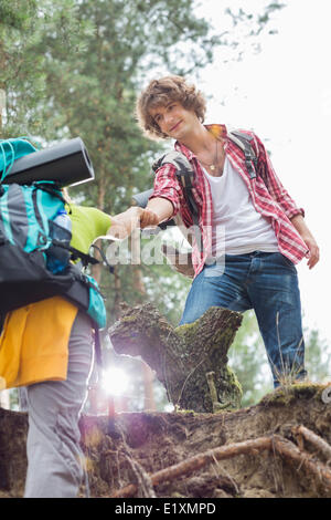 Low angle view of male hiker helping woman escalade en falaise à forest Banque D'Images