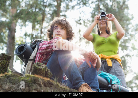 Young female hiker photographing par appareil photo numérique tandis que l'homme à l'écart dans la forêt Banque D'Images