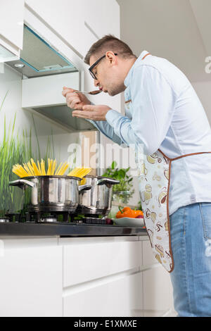 Mid-adult man nourriture d'échantillon en cours de cuisson dans la cuisine Banque D'Images