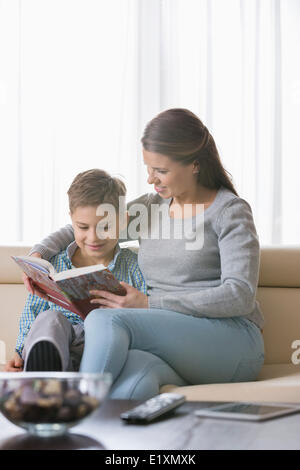 Mère et fils reading book on sofa at home Banque D'Images