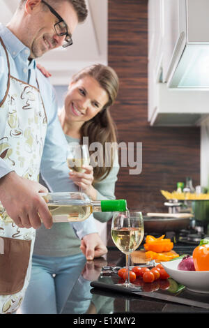 Homme heureux de verser le vin blanc dans le verre pendant la cuisson avec cuisine à femme Banque D'Images