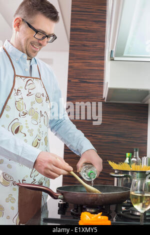 Homme heureux d'ajouter le vin blanc dans la casserole pendant la cuisson dans la cuisine Banque D'Images