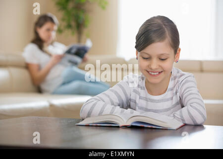 Smiling girl reading book avec en arrière-plan à la maison mère Banque D'Images