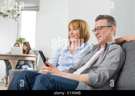 Les parents de regarder la télévision sur un canapé avec des enfants à l'aide d'ordinateur portable en arrière-plan Banque D'Images