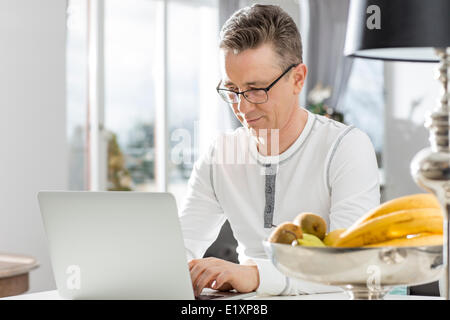 Mature man using laptop at table in house Banque D'Images