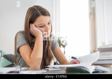 Bored girl studying at table in house Banque D'Images