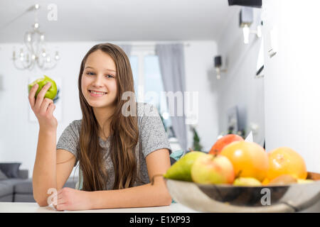 Portrait of smiling girl holding apple tout en étant assis à table dans la chambre Banque D'Images