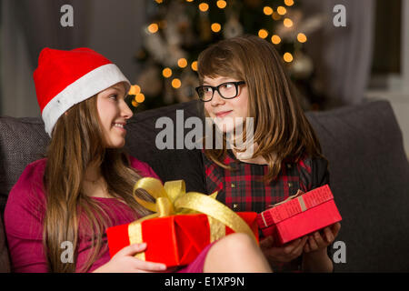 Les sœurs avec des cadeaux de Noël à l'un l'autre sur le canapé Banque D'Images