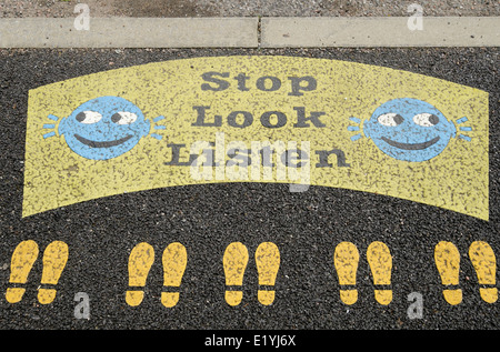 Arrêter de regarder écouter signe avec smileys et footprints peint sur un trottoir en bordure de route près d'une école primaire de passage ci-dessus. Royaume-uni Grande-Bretagne Banque D'Images