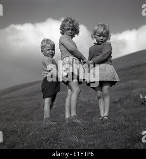 Années 1950, un portrait historique par J Allan Paiement de trois jeunes enfants du pays se tenant ensemble sur une colline se tenant la main. Banque D'Images