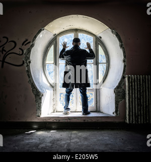 Un homme en face d'une ancienne fenêtre dans un immeuble abandonné Banque D'Images