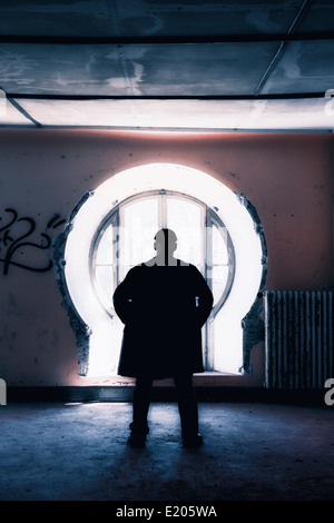 Silhouette d'un homme en face d'une fenêtre dans un vieux bâtiment abandonné Banque D'Images