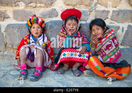 Trois enfants en habit traditionnel des Indiens Quechua s'asseoir devant un mur, Ollantaytambo, vallée de l'Urubamba, au Pérou Banque D'Images