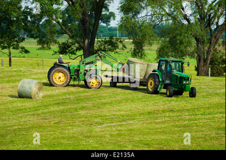 Farmer Chargement des bobines de foin en balles rondes sur un tracteur avec remorque à plateau Banque D'Images