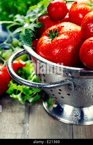 Les tomates fraîches (dans une passoire métallique) et d'herbes sur une table en bois Banque D'Images