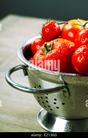 Les tomates fraîches (dans une passoire métallique) et d'herbes sur une table en bois Banque D'Images