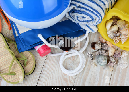 Un groupe d'éléments pour une journée à la plage, sandales, ballon de plage, sac, lunettes de soleil, serviette et seau de sable avec des coquillages Banque D'Images