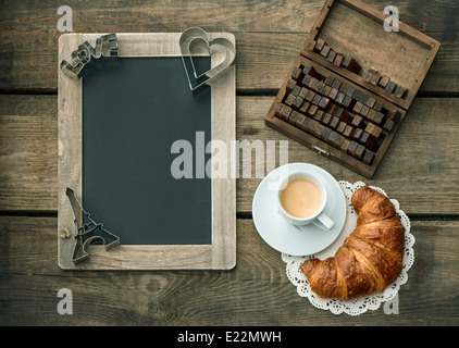 Tasse de café noir avec un croissant, un tableau noir et coeur décor sur fond de bois rustique. Banque D'Images