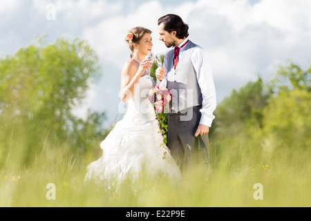 Mariage mariée et le marié dans un pré, avec bouquet, champagne et verres Banque D'Images