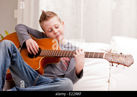 Petit garçon qui joue de la guitare sur un canapé dans son salon Banque D'Images