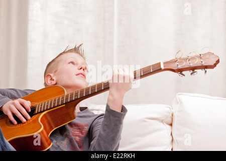 Petit garçon qui joue de la guitare sur un canapé dans son salon Banque D'Images