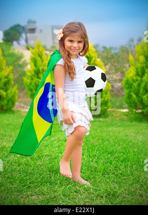 Happy cheerful girl Playing with ball sur l'arrière-cour en journée ensoleillée, grand drapeau national du championnat de football du Brésil, concept Banque D'Images