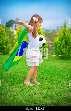 Happy cheerful girl Playing with ball sur l'arrière-cour en journée ensoleillée, grand drapeau national du championnat de football du Brésil, concept Banque D'Images