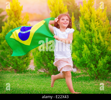 Happy little fan de football, jolie petite fille courir sur le parc national de brandir le drapeau avec le Brésil sur le vent, la petite enfance sportive Banque D'Images