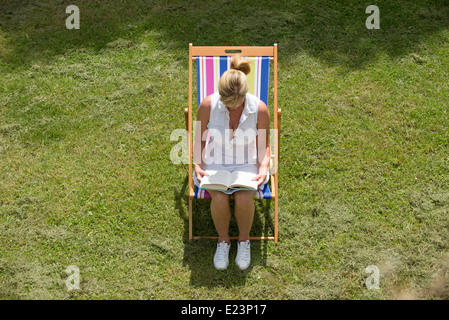 Femme assise sur une chaise en lisant un livre Banque D'Images