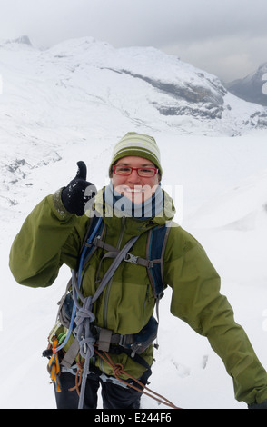 Une dame mountaineer donnant un joyeux Thumbs up sign haut dans les Alpes Suisses Banque D'Images