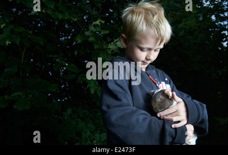 Portrait d'enfant garçon blond tenant un cochon à l'extérieur Banque D'Images