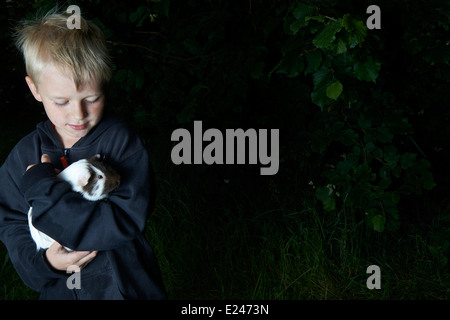 Portrait d'enfant garçon blond tenant un cochon à l'extérieur Banque D'Images