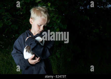 Portrait d'enfant garçon blond tenant un cochon à l'extérieur Banque D'Images