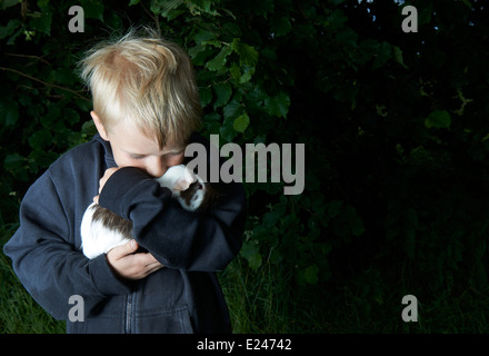 Portrait d'enfant garçon blond tenant un cochon à l'extérieur Banque D'Images