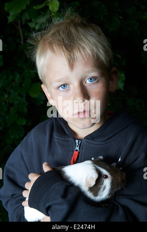 Portrait d'enfant garçon blond tenant un cochon à l'extérieur Banque D'Images