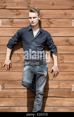 Beau jeune homme blond se tenant debout à l'extérieur contre le mur de bois looking at camera Banque D'Images