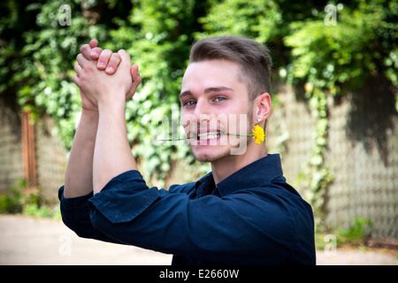 Beau jeune homme avec une fleur dans la bouche des mains. À l'extérieur Banque D'Images